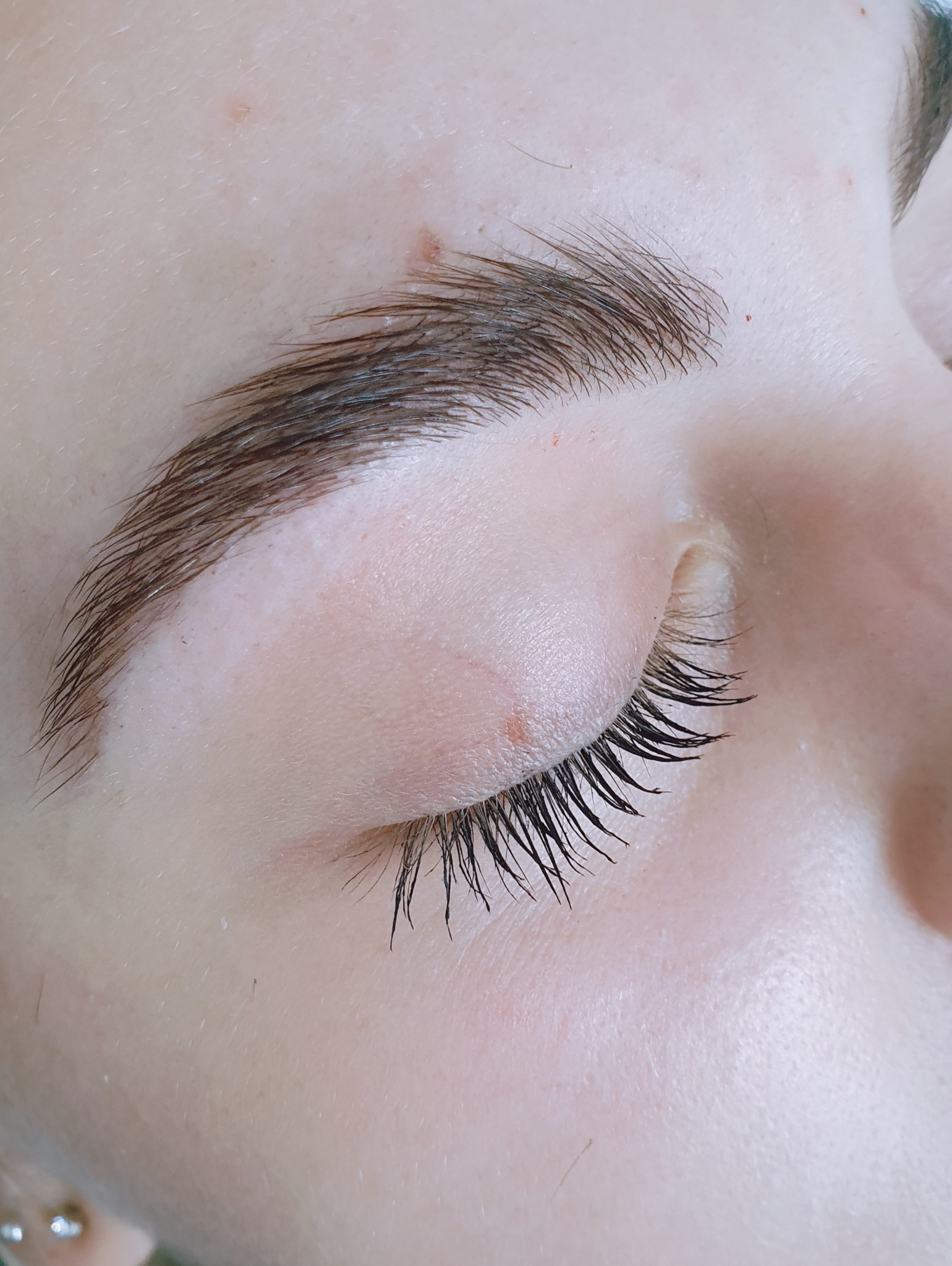 Zamknięte oko z widocznymi, przedłużonymi czarnymi rzęsami i naturalnie ukształtowanymi brwiami w ciepłym oświetleniu.