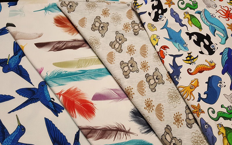 Stosy materiałów z nadrukami: kolibry, pióra, misie i morskie zwierzęta w stylu cartoon.