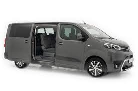 Szary minivan Toyota Proace Verso z otwartymi przesuwnymi drzwiami bocznymi, widoczne fotele wewnątrz, na białym tle.