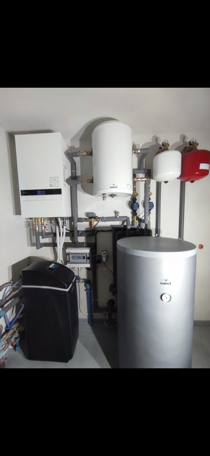 Kompletna kotłownia z zasobnikiem ciepłej wody, zmiękczaczem wody i rozbudowaną instalacją hydrauliczną z rurami w izolacji.