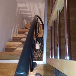 Padre złota rączka - Schody drewniane z czarną balustradą, widok z góry, fragment podłogi i buta osoby fotografującej w kadrze.