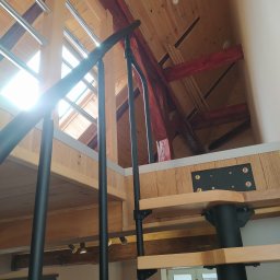Padre złota rączka - Wnętrze domu z drewnianym stropem i schodami spiralnymi z czarną balustradą, widok z dołu na poddasze z oknem dachowym.