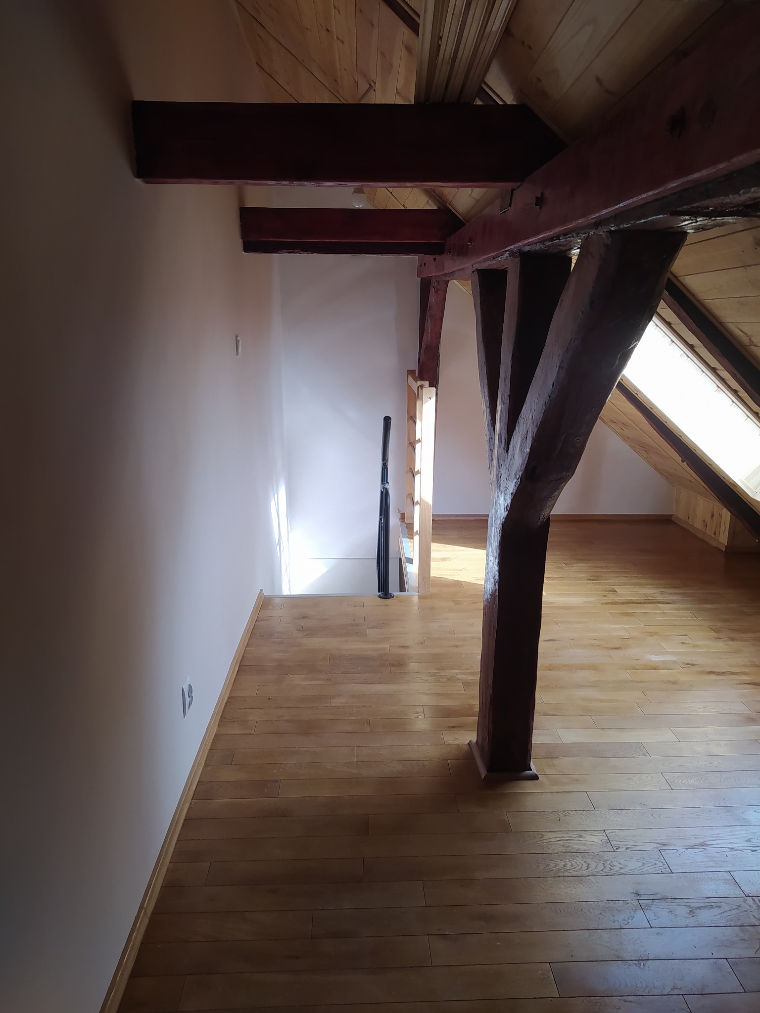 Poddasze po remoncie: jasna podłoga z paneli, drewniane belki konstrukcyjne i białe ściany, widoczne gniazdka elektryczne przy podłodze.