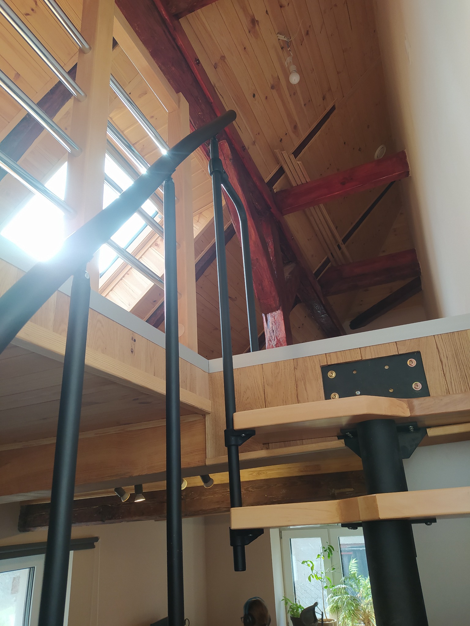 Wnętrze domu z drewnianym stropem i schodami spiralnymi z czarną balustradą, widok z dołu na poddasze z oknem dachowym.