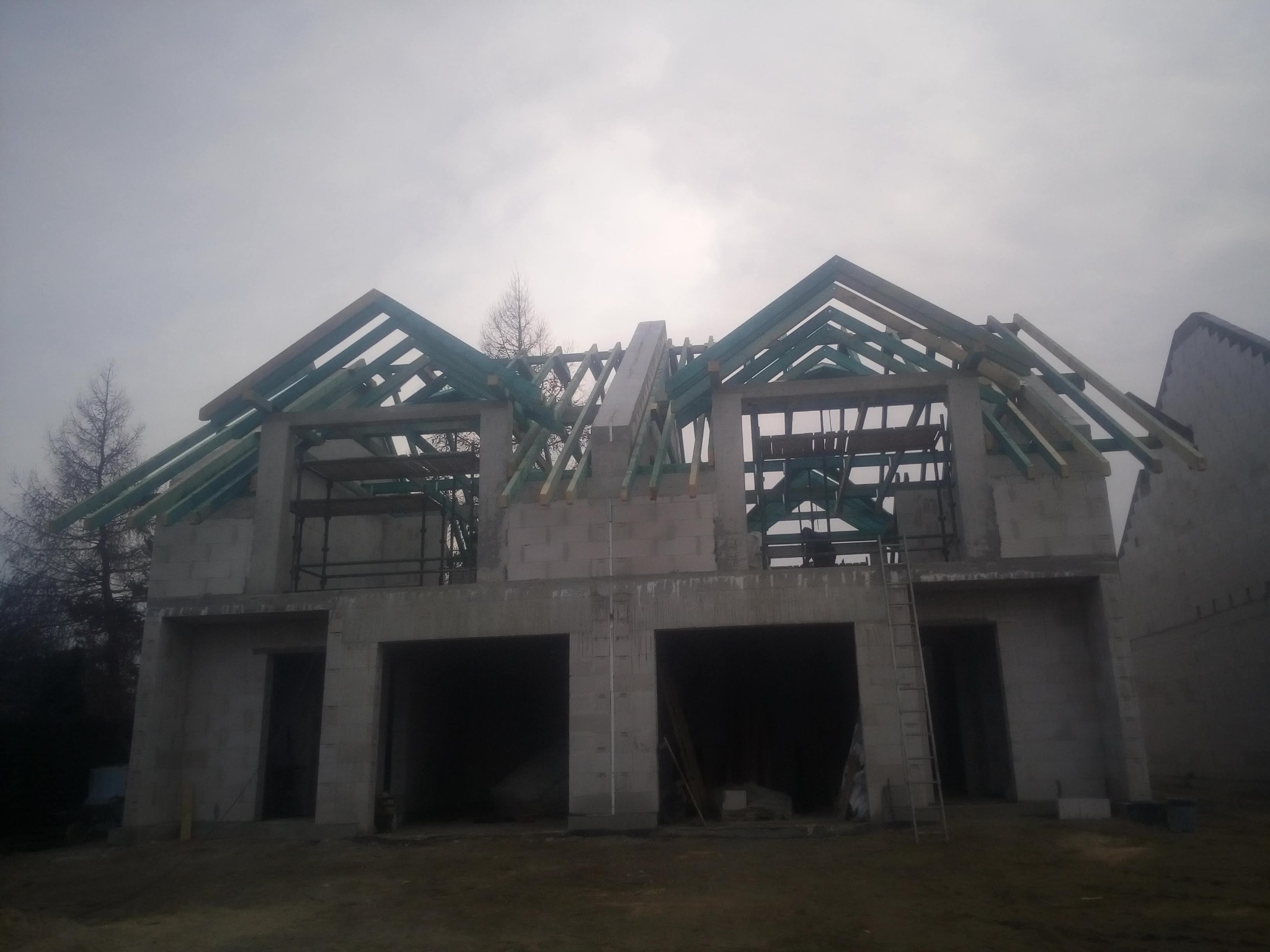 Surowy stan bliźniaka z betonu komórkowego z drewnianą konstrukcją dachu, widok na budynek w pochmurny dzień.