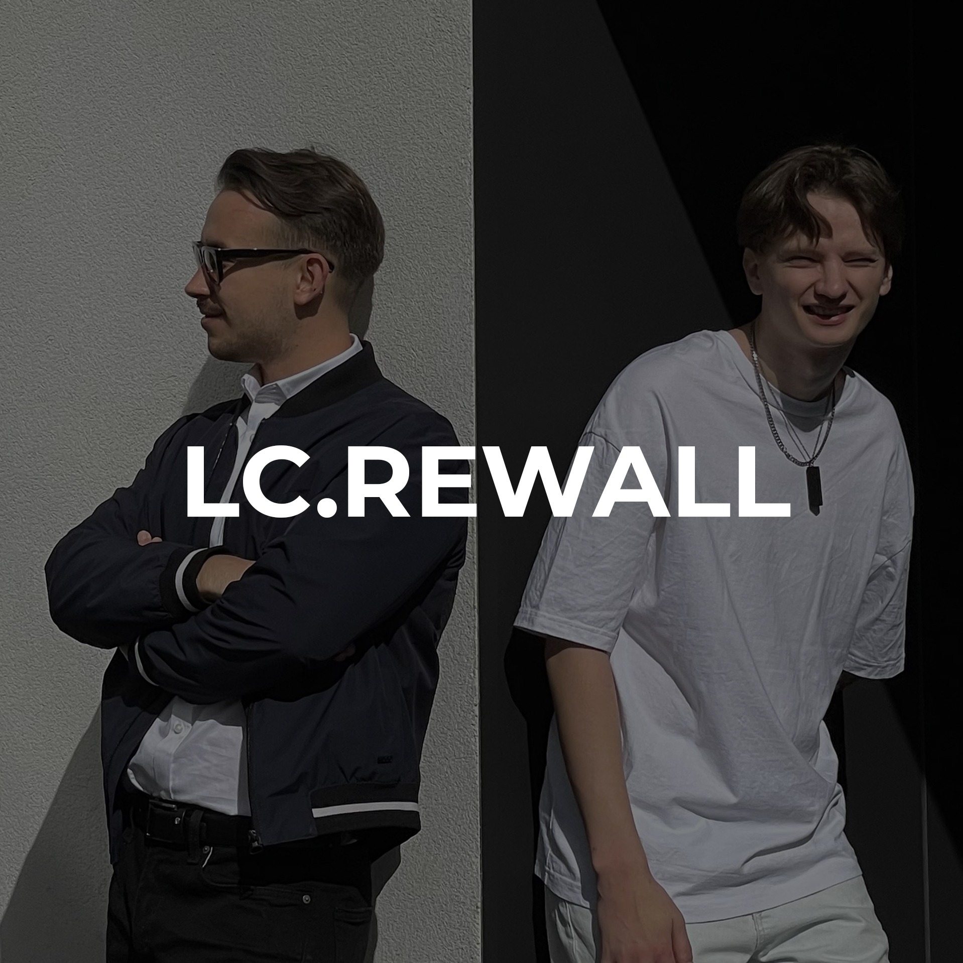 Portret dwóch mężczyzn na tle podzielonym na szaro-białą ścianę i czarne tło, z nałożonym tekstem 'LC.REWALL'. Jeden mężczyzna w okularach, koszuli i kurtce, drugi w białym t-shircie i łańcuszku.