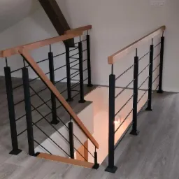Nowoczesne schody z czarnymi metalowymi słupkami i drewnianą poręczą, widok z góry na szare panele podłogowe.