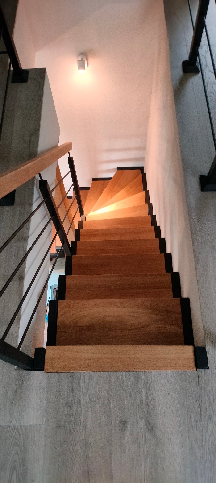 Drewniane schody z metalową balustradą, widok z góry, stopnie oświetlone ciepłym światłem, nowoczesny design.