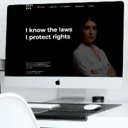Ekran komputera iMac prezentujący stronę internetową kancelarii prawnej z czarnym tłem, białym tekstem 'I know the laws I protect rights' i zdjęciem prawniczki w białej koszuli z założonymi rękami,...