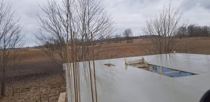 Zalany betonem fundament z otworami, widok z góry na tle polskiego krajobrazu z drzewami bez liści i pochmurnym niebem.