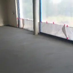 Świeżo wylana, gładka posadzka w surowym wnętrzu, zabezpieczona folią okienna z ostrzeżeniem na kartce.