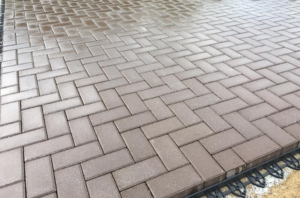 Ułożona, brązowa kostka brukowa w jodełkę, lekko mokra, z widocznym obrzeżem z tworzywa sztucznego.