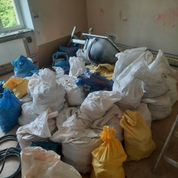 Wywóz gruzu - Stos worków z gruzem w pomieszczeniu w trakcie remontu, widoczna wanna, drabina i przewody elektryczne, ściany z śladami po instalacjach.