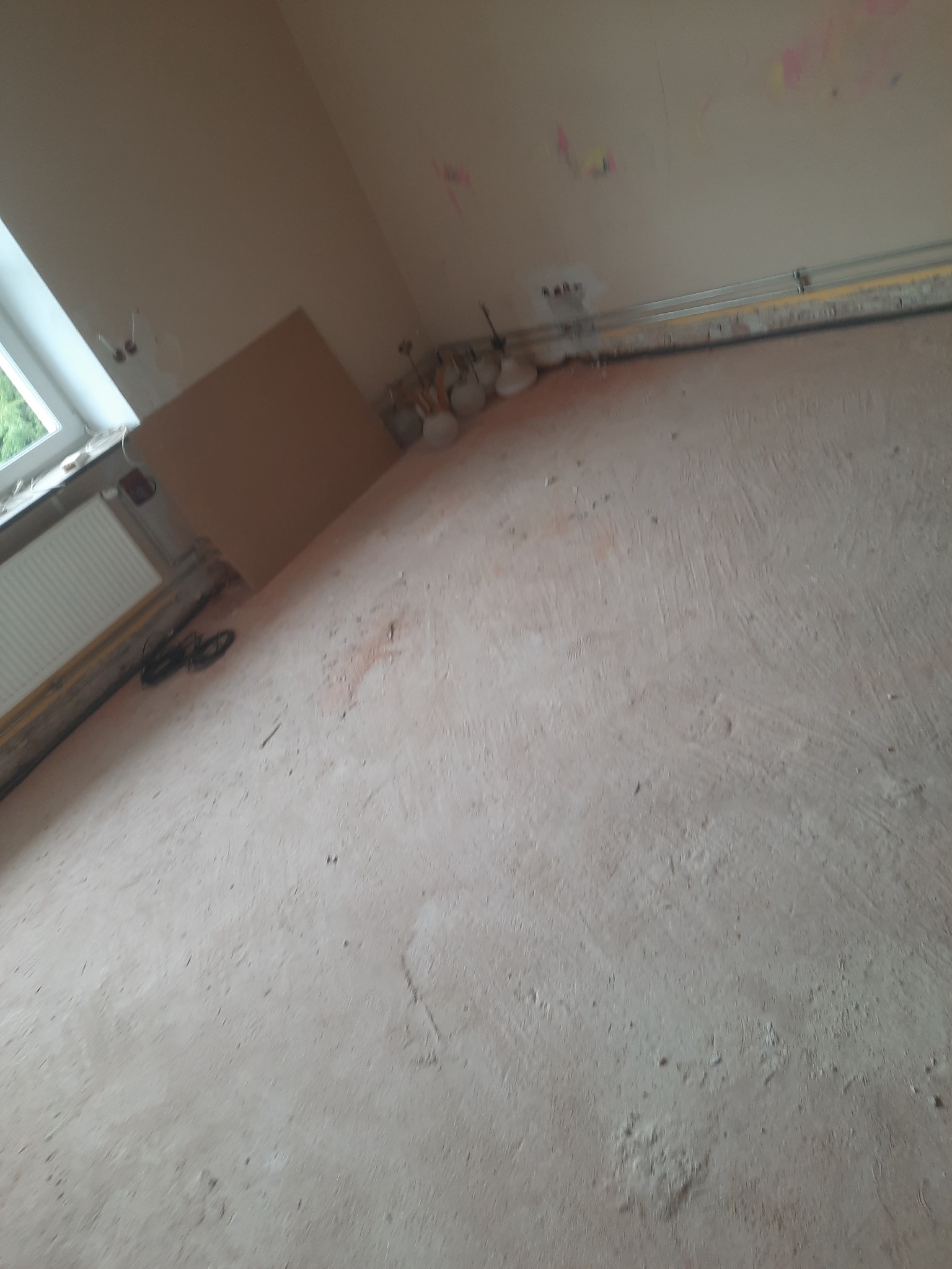 Przygotowane podłoże pod wylewkę w pomieszczeniu z widocznymi przewodami elektrycznymi i fragmentem okna.