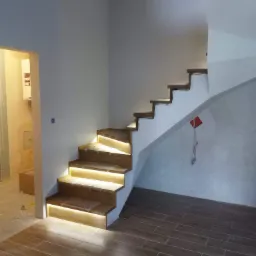 Drewniane schody z podświetleniem LED w trakcie montażu, widoczne zabezpieczenia na stopniach i przewody na podłodze.