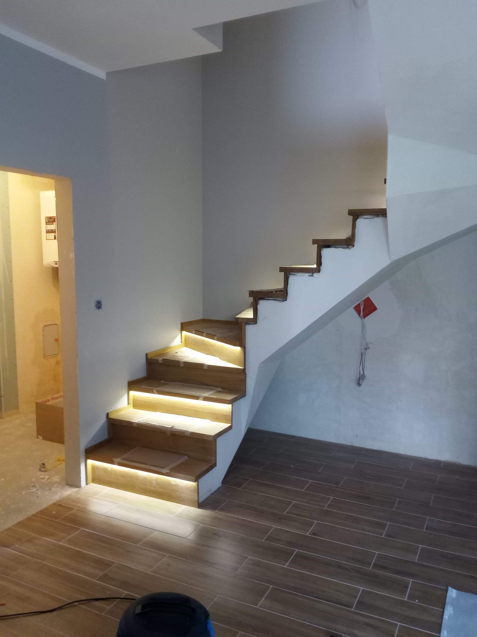 Drewniane schody z podświetleniem LED w trakcie montażu, widoczne zabezpieczenia na stopniach i przewody na podłodze.