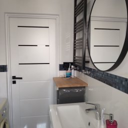 HouseGello Aleh Kapranau - Nowoczesna łazienka z białą umywalką, baterią, dozownikiem mydła w kolorze fuksji, grzejnikiem drabinkowym w kolorze czarnym i lustrem w czarnej ramie. Na ścianie dekoracyjny pas mozaiki...