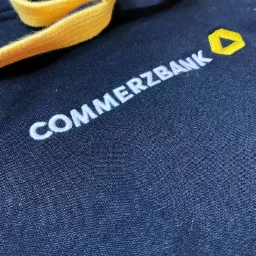 Granatowa bluza z kapturem, z wyhaftowanym białym napisem Commerzbank i żółtym logo, oraz żółtym sznurkiem kaptura.