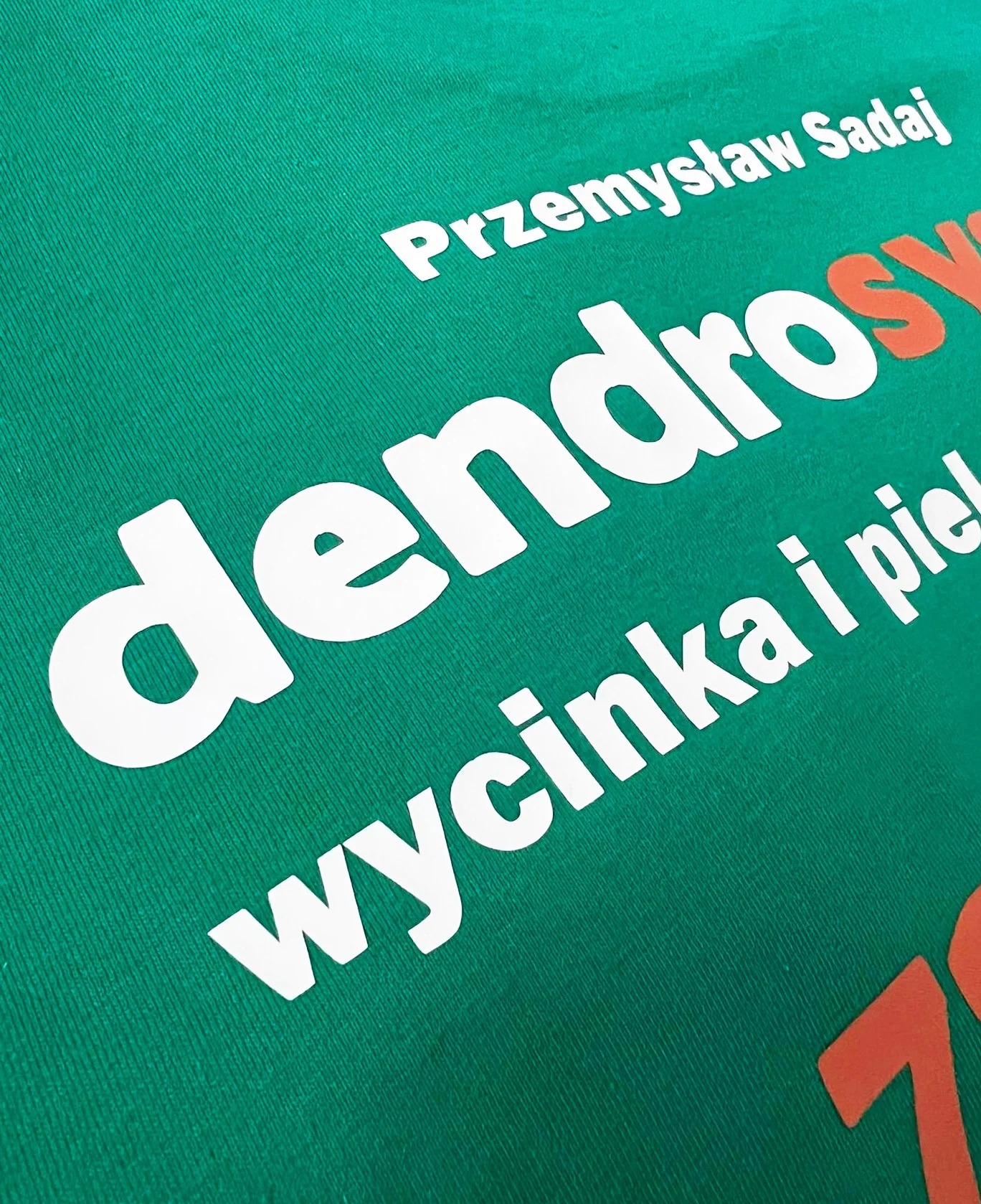 Zielona koszulka z białym i pomarańczowym nadrukiem tekstu 'Przemysław Sadaj dendros wycinka i pielęgnacja'
