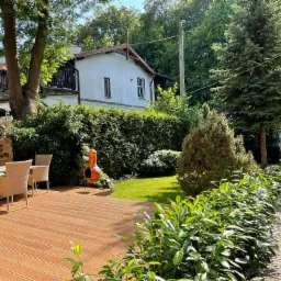 Nowoczesny taras kompozytowy z meblami ogrodowymi i kominkiem zewnętrznym w Gdyni, otoczony zielenią i kamienną ścieżką.