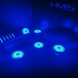 Niebieskie światło oświetla przyrządy do ćwiczeń z logo HMS, prawdopodobnie do rehabilitacji lub terapii światłem.