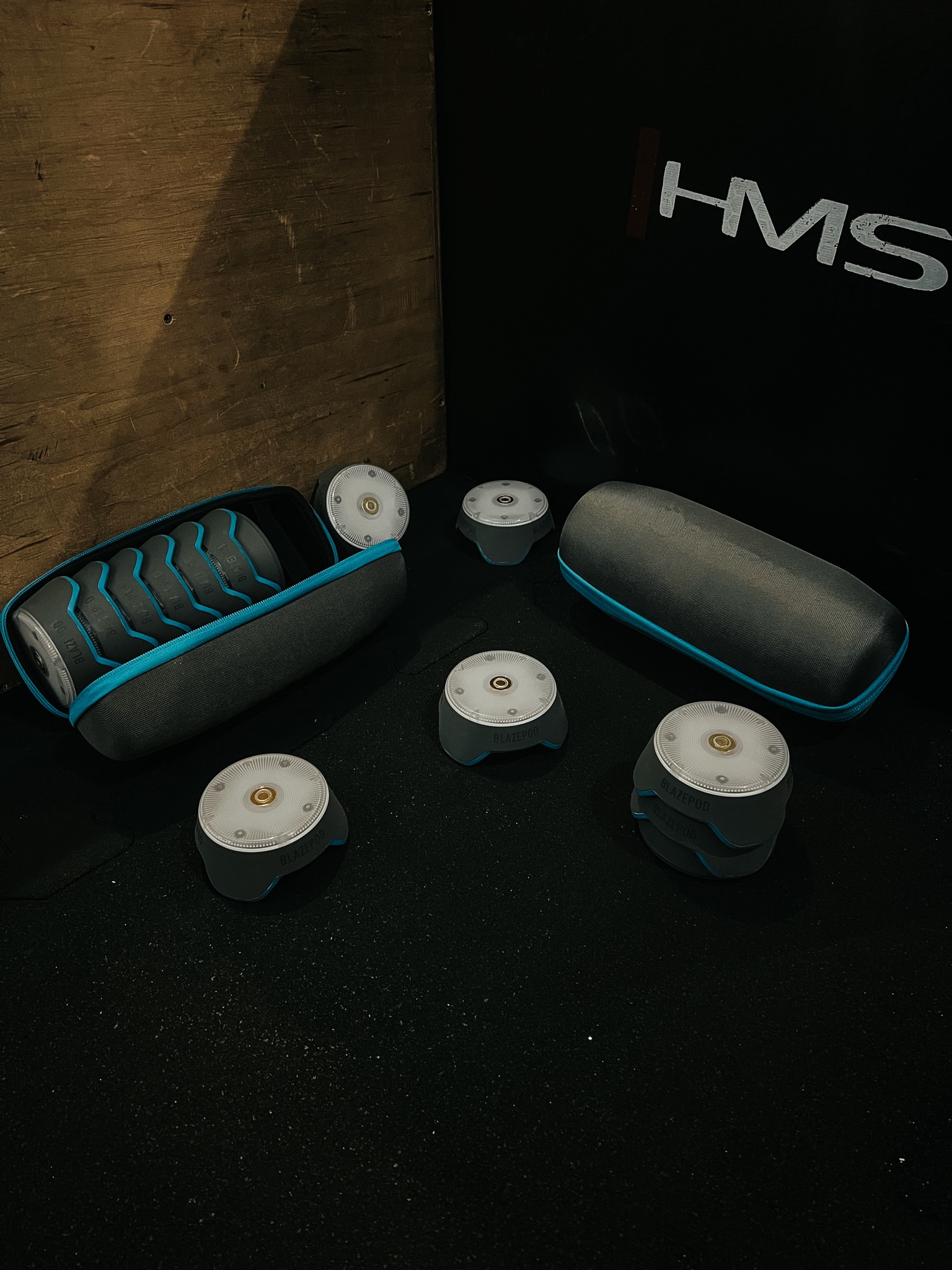 Zestaw urządzeń BlazePod do treningu reakcji i zwinności, w futerale i poza nim, na ciemnym tle z logo HMS.