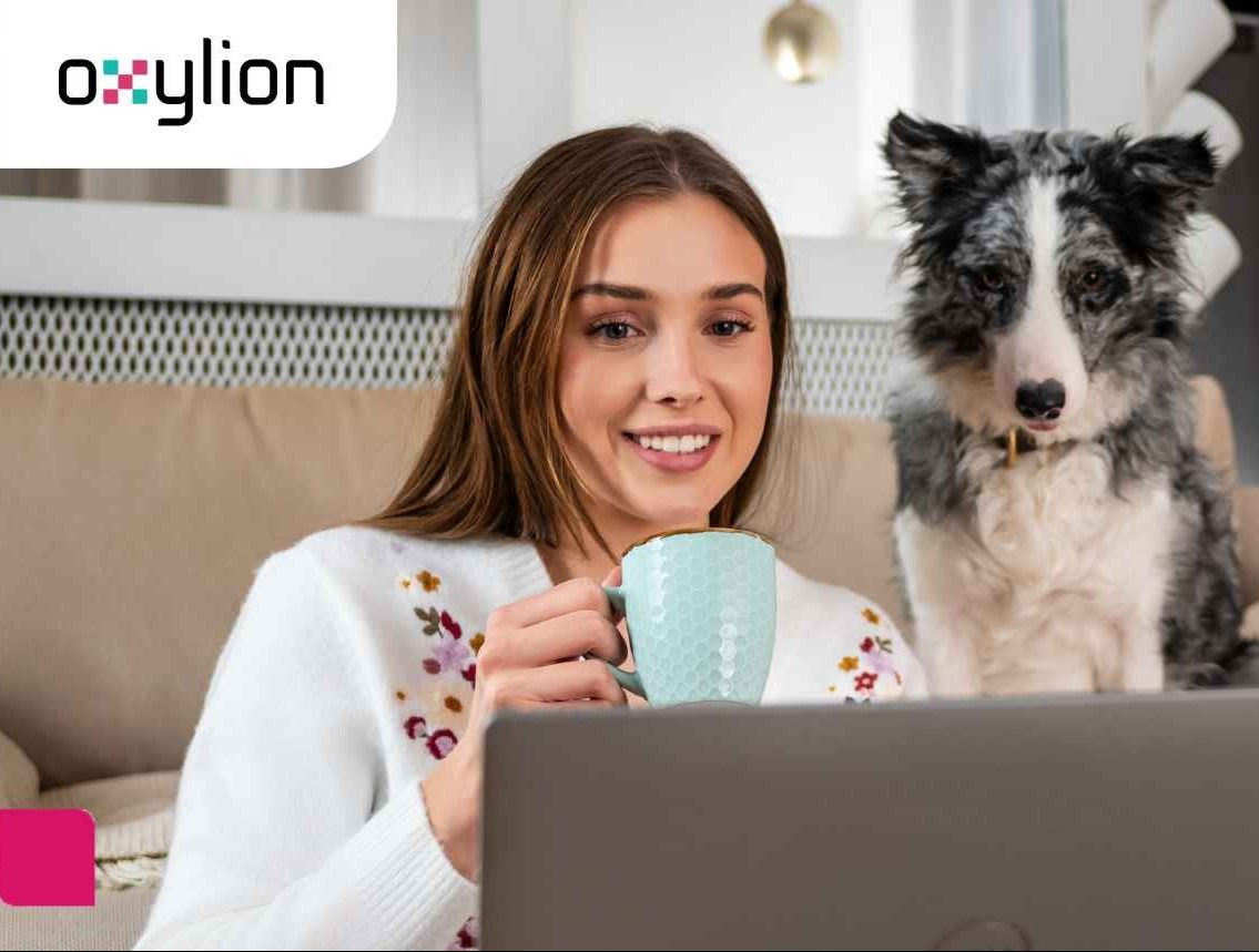 Kobieta z kubkiem i psem siedzi na kanapie przed laptopem. W tle logo firmy, sugerujące usługi dostępu do sieci.