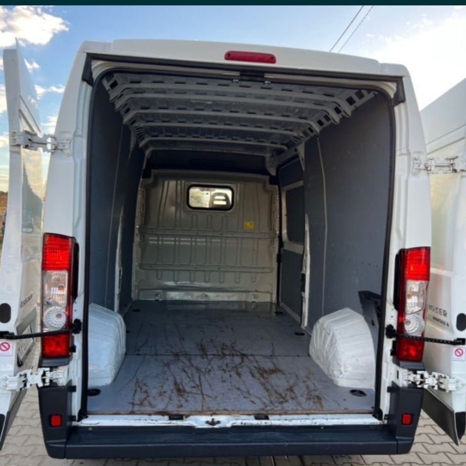 Wnętrze pustej, białej furgonetki z otwartymi tylnymi drzwiami, widok z tyłu, brudna podłoga przestrzeni ładunkowej.