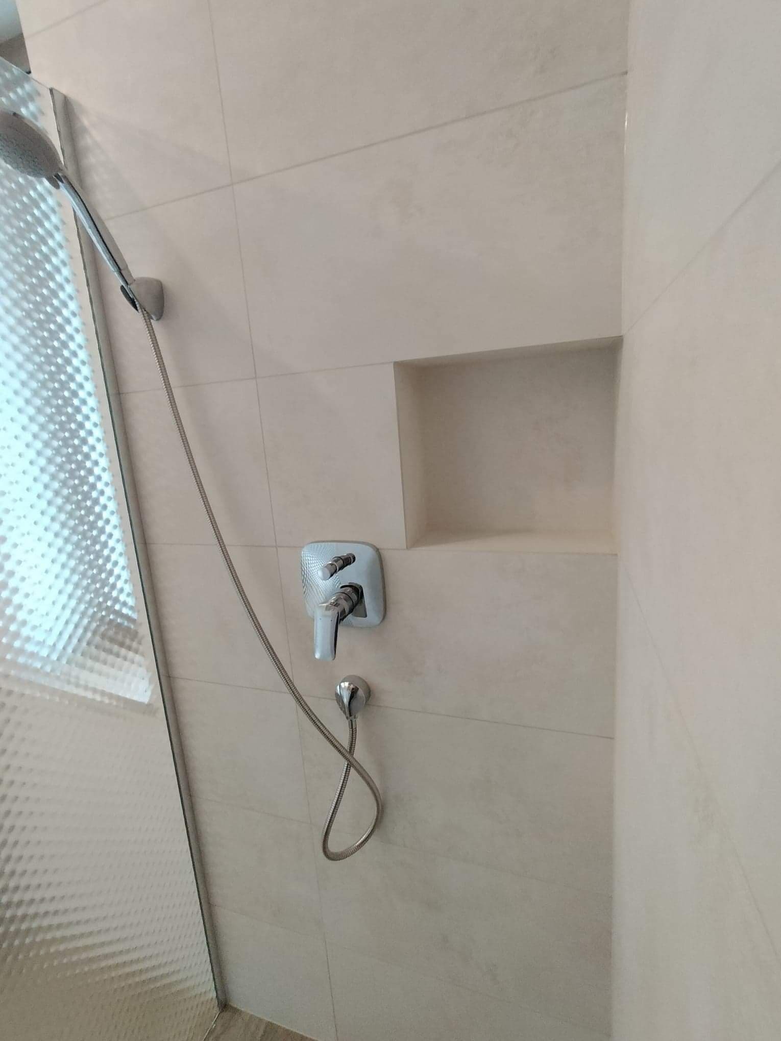 Beżowa łazienka z kabiną prysznicową, chromowaną armaturą i wnęką w ścianie wykończoną płytkami ceramicznymi.