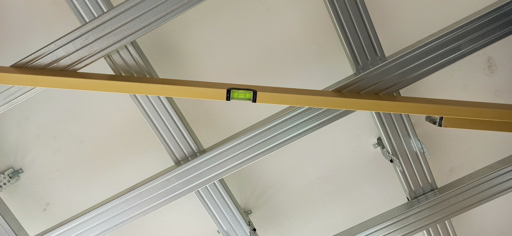 Stelaż sufitu podwieszanego z profili metalowych, wypoziomowany poziomicą w kolorze złotym.