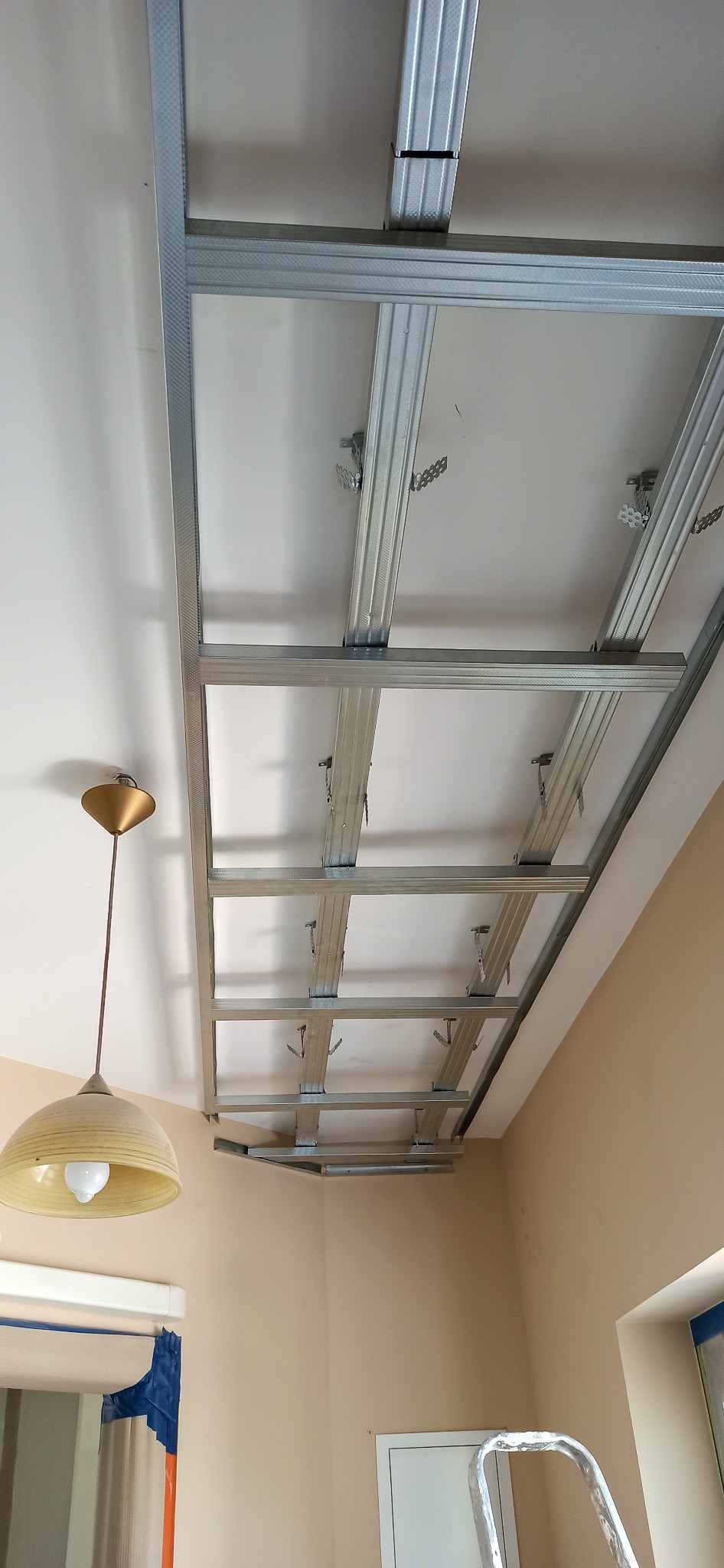 Stelaż sufitu podwieszanego z płyt kartonowo-gipsowych, widok od dołu z wiszącą lampą i fragmentem drabiny