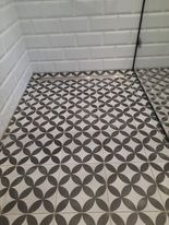 Wykończona posadzka prysznicowa z odpływem liniowym w Grodzisku Mazowieckim. Ciemnoszara mozaika o wzorze kwiatowym kontrastuje z jasnymi, cegiełkowymi płytkami ściennymi.