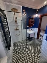 Nowoczesna łazienka z kabiną prysznicową typu walk-in, czarno-białą mozaiką na podłodze, białymi płytkami imitującymi cegłę na ścianach, fragmentem ściany pomalowanej na granatowo i okrągłym...
