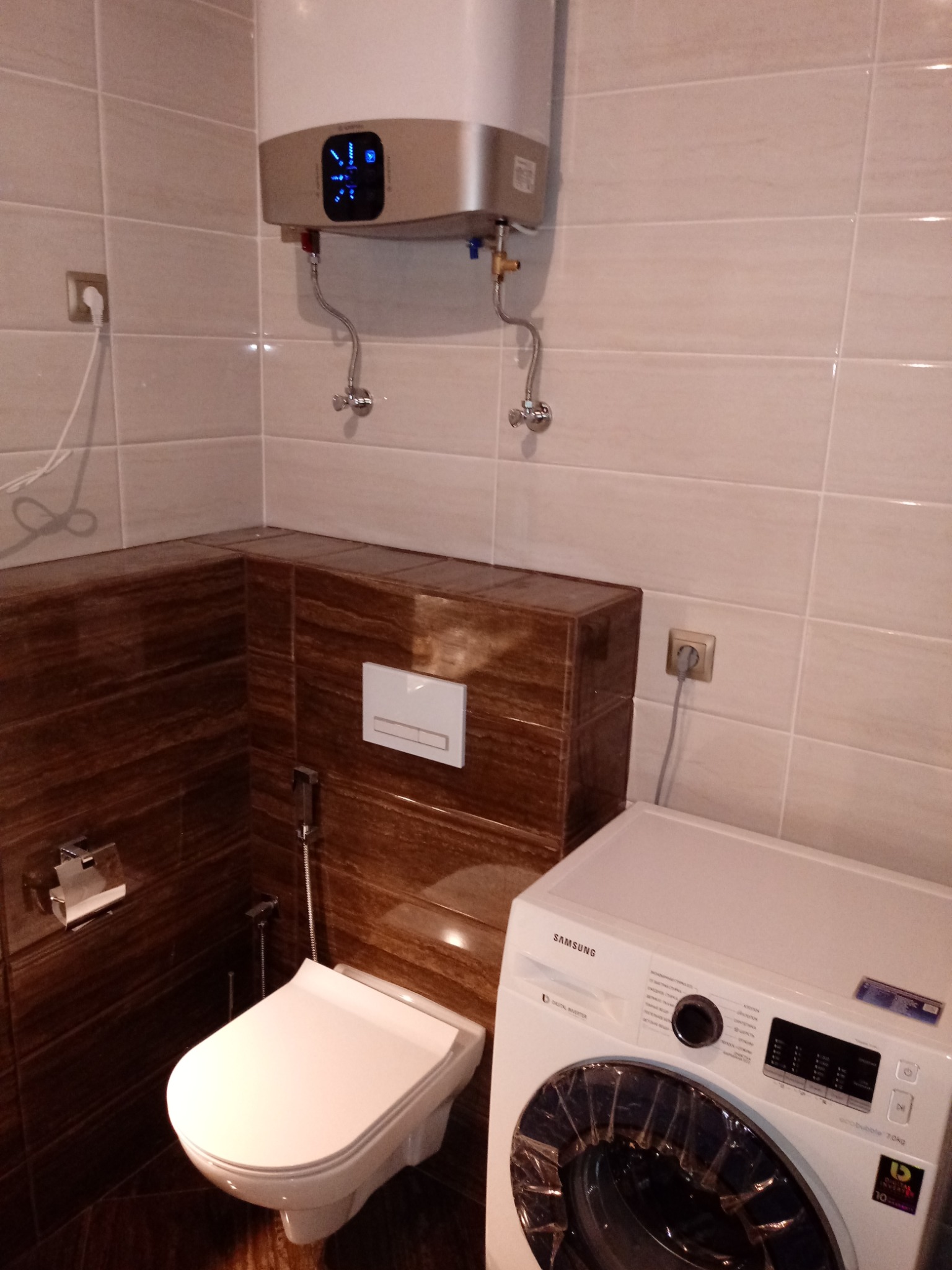 Nowoczesna łazienka z podwieszaną toaletą, bojlerem elektrycznym i pralką Samsung, wykończona płytkami w odcieniach beżu i brązu.