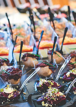Ustawione w rzędach przekąski: buraczane carpaccio z kiełkami i orzechami na czarnych łyżkach, pasztet w przezroczystych naczyniach z czarnymi widelczykami oraz inne finger foody.