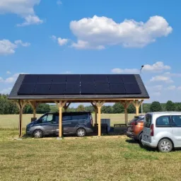 Zadaszenie parkingowe z drewnianą konstrukcją, pokryte panelami fotowoltaicznymi, chroniące zaparkowane samochody w słoneczny dzień.