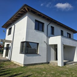 ELBUD PARTNER MARCIN MIGA I ILONA BUDNIACZYŃSKA S.C. - Nowoczesny dom jednorodzinny z jasną elewacją w trakcie prac wykończeniowych, widoczne elementy konstrukcyjne tarasu oraz fragmenty niezagospodarowanego terenu wokół budynku.