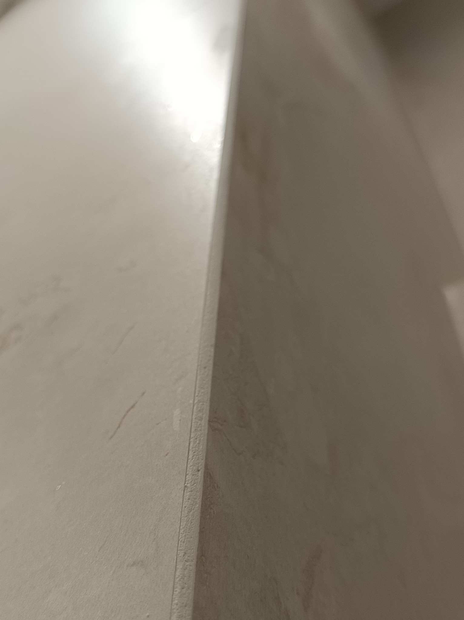 Fragment ściany wykończonej gładzią, widoczne delikatne smugi i niedoskonałości pod światło.