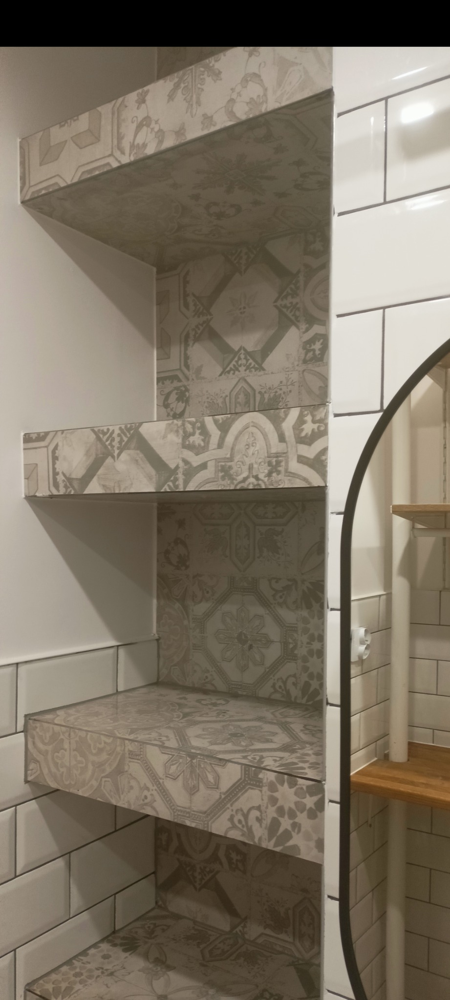 Narożna półka z płytek ceramicznych w łazience, wzór patchworkowy w odcieniach szarości i beżu, białe płytki ścienne w tle.