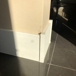 Glib Kolbasin - Świeżo pomalowana ściana i listwa przypodłogowa w słonecznym świetle w Warszawie, z ciemną, błyszczącą podłogą z płytek.