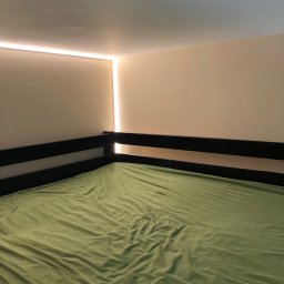 Glib Kolbasin - Pokój z łóżkiem piętrowym, świeżo pomalowane ściany w odcieniach beżu i biała listwa LED pod sufitem, oświetlająca górną część ściany.
