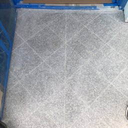 Glib Kolbasin - Szara, wzorzysta podłoga z płytek ceramicznych ułożonych w karo, zabezpieczona niebieską taśmą malarską przy progu drzwi.