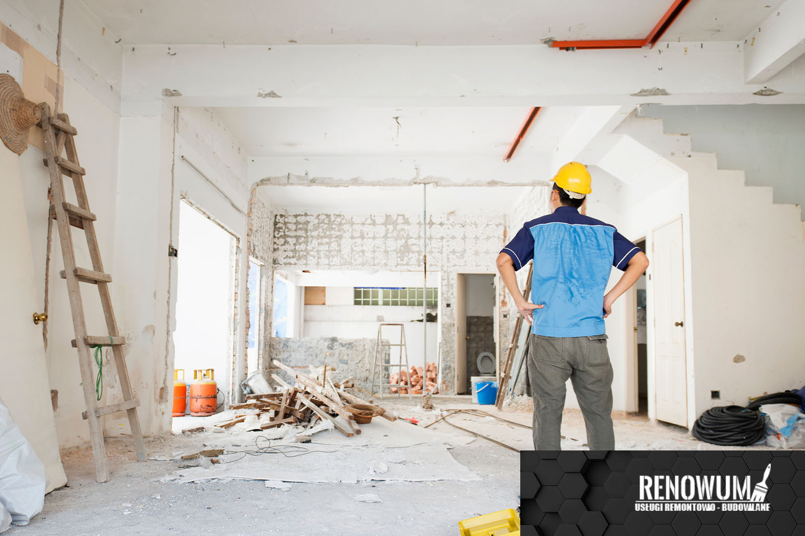 Mężczyzna w kasku, stojący tyłem, obserwuje wnętrze w trakcie rozbiórki, widoczne ślady po skuciu płytek, drewniane elementy, drabina i butle gazowe w tle.