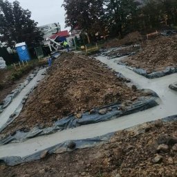 Dawid Kaleta - Wylane fundamenty pod budowę domu, widoczne szalunki i pryzmy ziemi, w tle betoniarka z wysięgnikiem i przenośna toaleta.