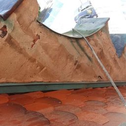 Dawid Kaleta - Zniszczona elewacja budynku z widocznymi ubytkami tynku i czerwonymi dachówkami na dachu, ujęcie z dołu.