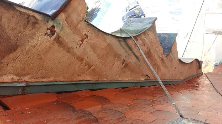 Zniszczona elewacja budynku z widocznymi ubytkami tynku i czerwonymi dachówkami na dachu, ujęcie z dołu.