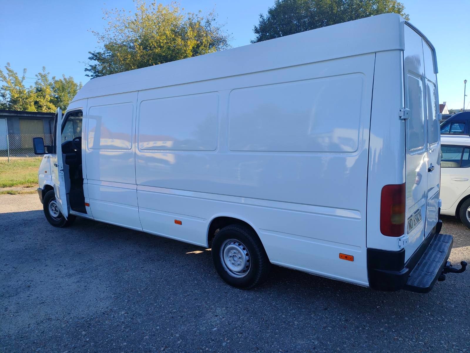 Biały samochód dostawczy z otwartymi drzwiami kierowcy, zaparkowany na zewnątrz, widok z boku i tyłu.