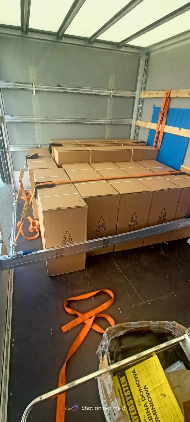 Wnętrze furgonetki wypełnionej kartonami zabezpieczonymi pomarańczowymi pasami transportowymi, widoczne elementy konstrukcyjne pojazdu.