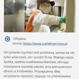 Pracownik w kombinezonie ochronnym, masce i rękawicach czyści powierzchnię w hali przemysłowej, dbając o higienę i bezpieczeństwo.