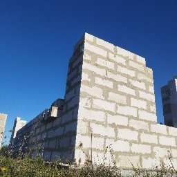 RealBud Hubert Hapka - Wznoszenie ścian domu z białych bloczków betonu komórkowego, widoczne spoiny zaprawy. Budowa w toku na tle błękitnego nieba i zielonej trawy.